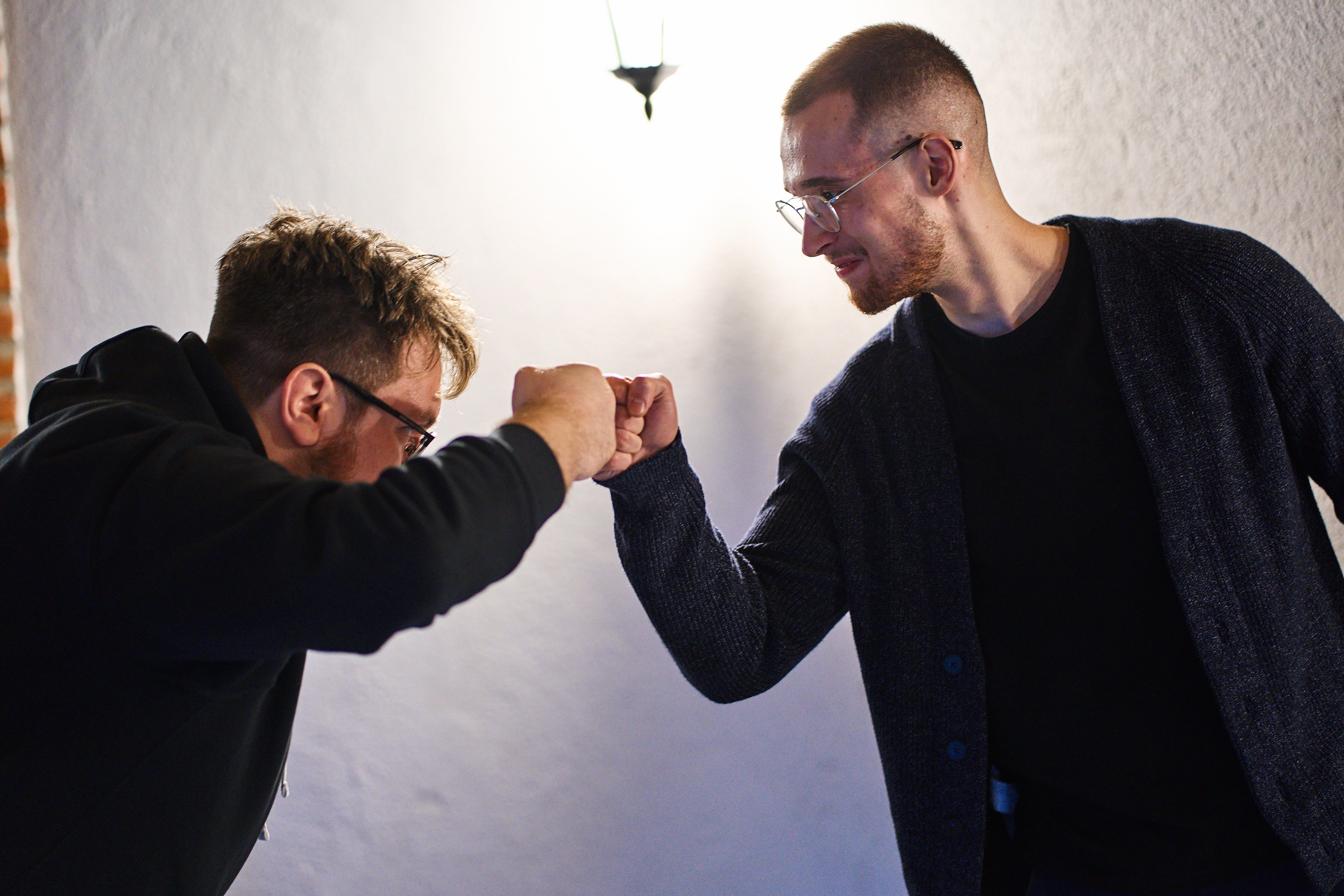 Two colleagues greeting each other with a friendly fist bump in a softly lit indoor setting.