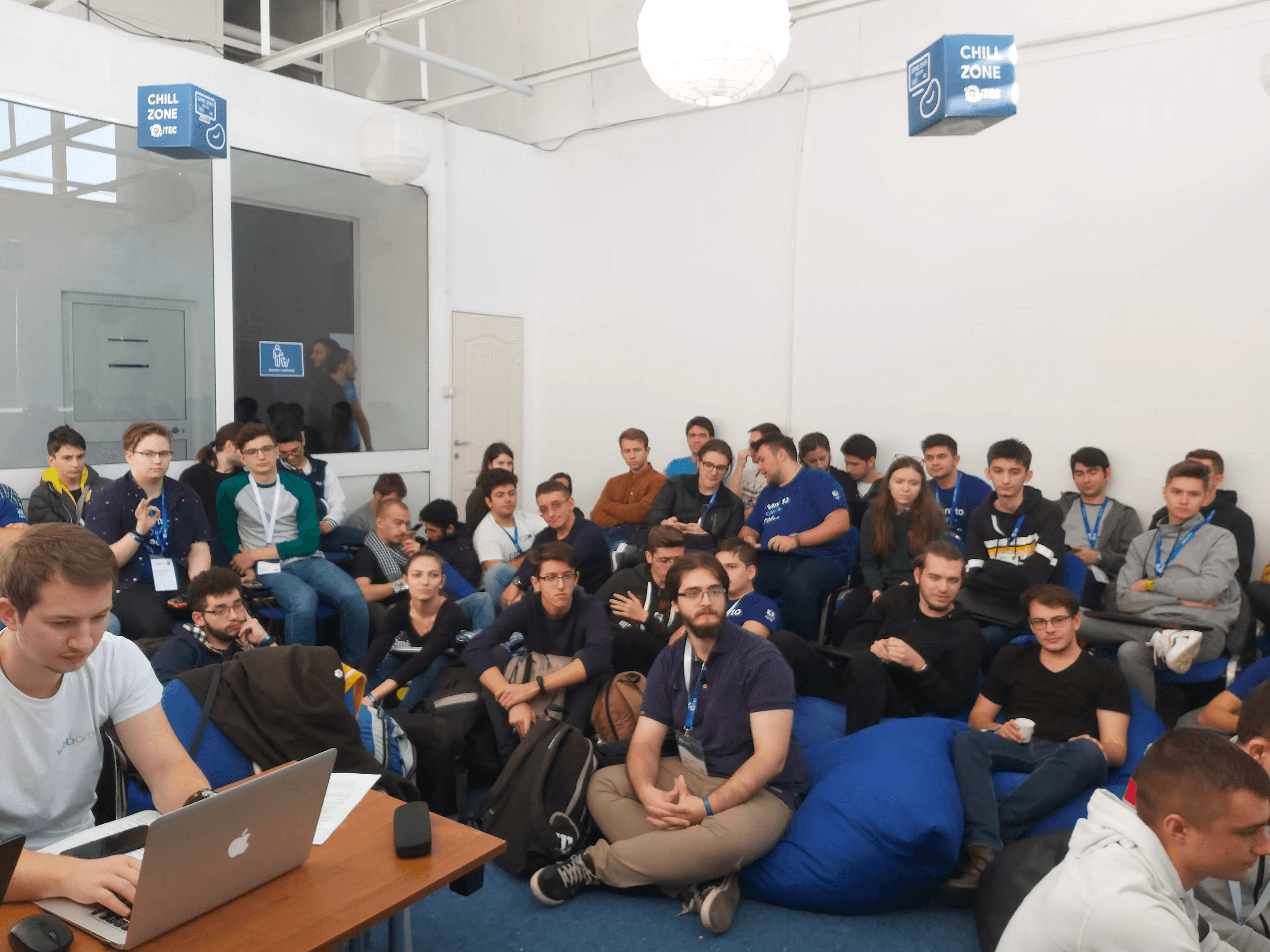 A large group of attendees seated closely together in a lounge area listening during a tech event session.