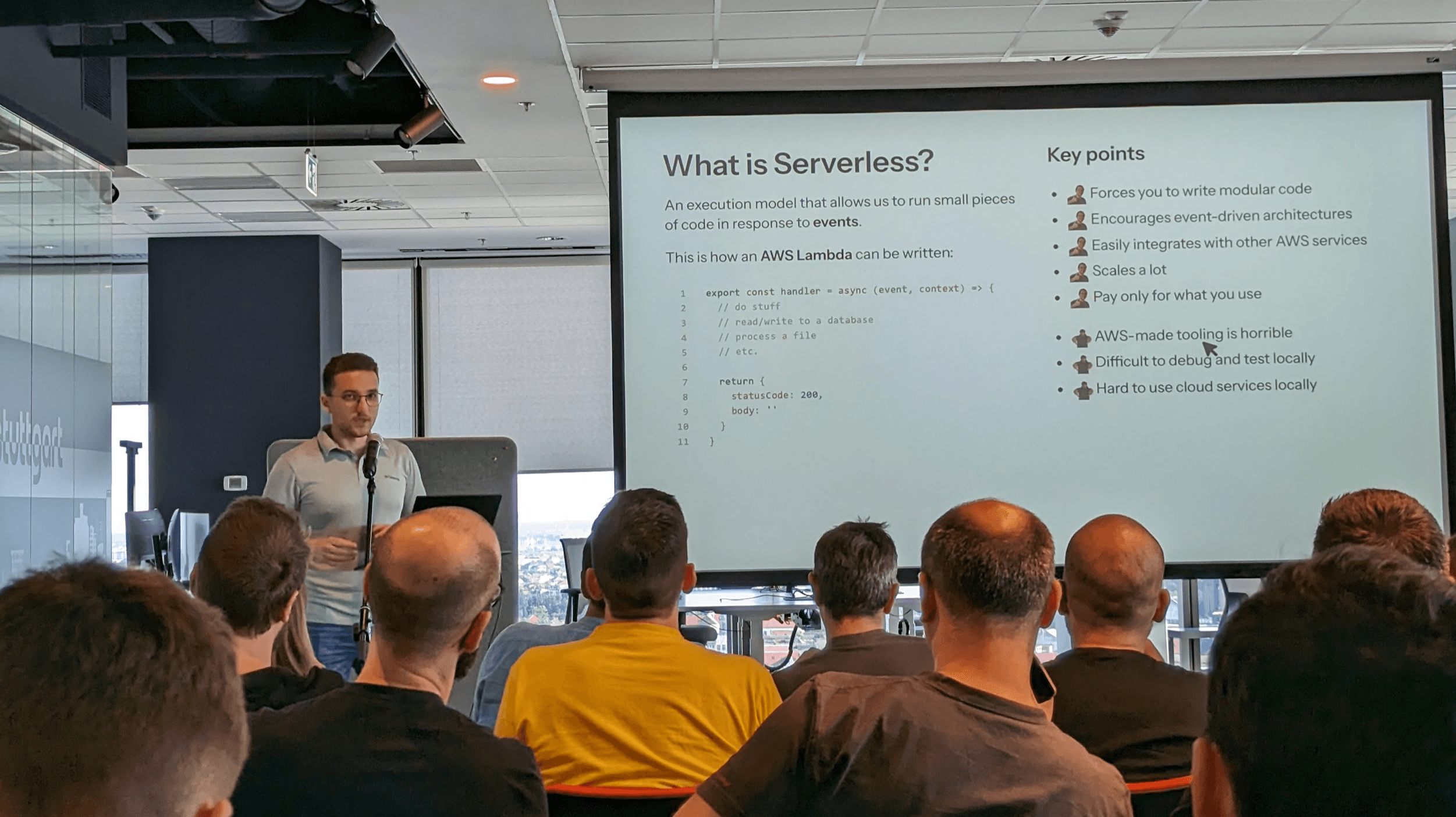 A presenter speaking into a microphone in front of a projected slide titled “What is Serverless?” during a technical meetup.